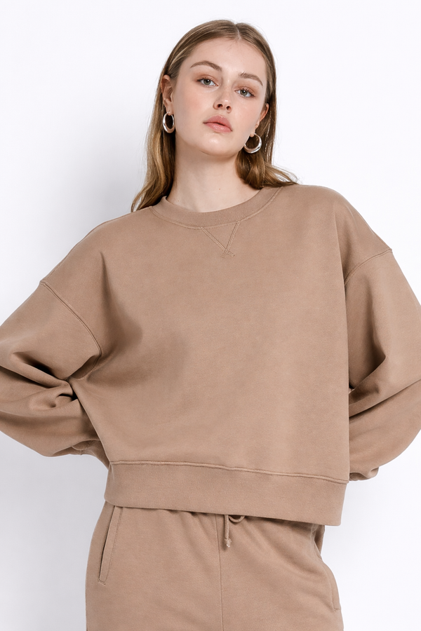 Model trägt camel-farbenes Sweatshirt mit lockerer Passform, Rundhalsausschnitt und breitem Saumbund, kombiniert mit passender Jogginghose.